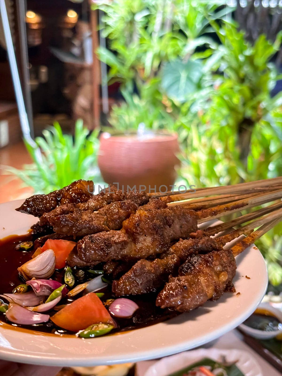 Lamb, mutton grilled skewer satay served with soy sauce sauce with sliced shallots, tomatoes, cucumber and cayenne pepper served in white plate by antoksena