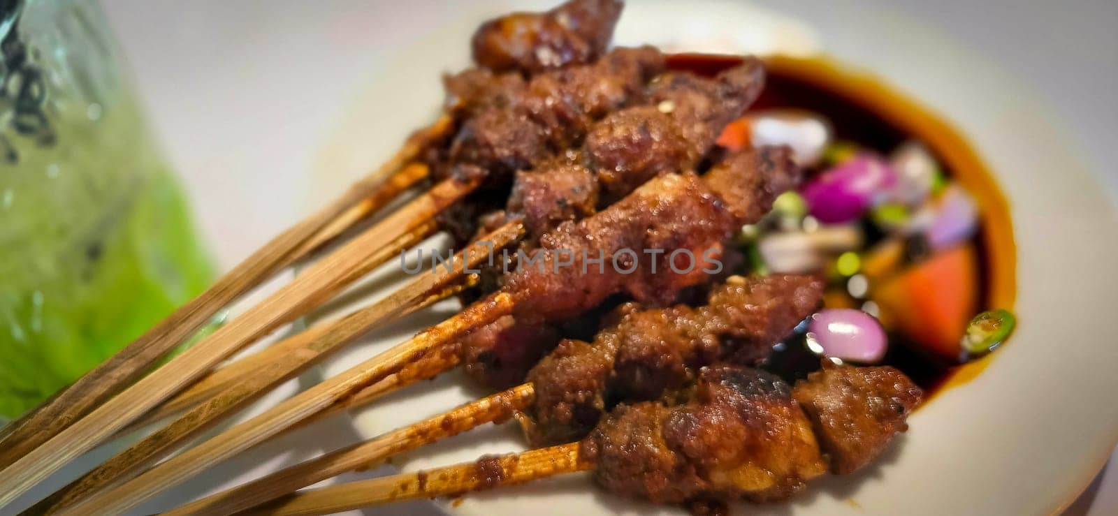 Lamb, mutton grilled skewer satay served with soy sauce sauce with sliced shallots, tomatoes, cucumber and cayenne pepper served in white plate