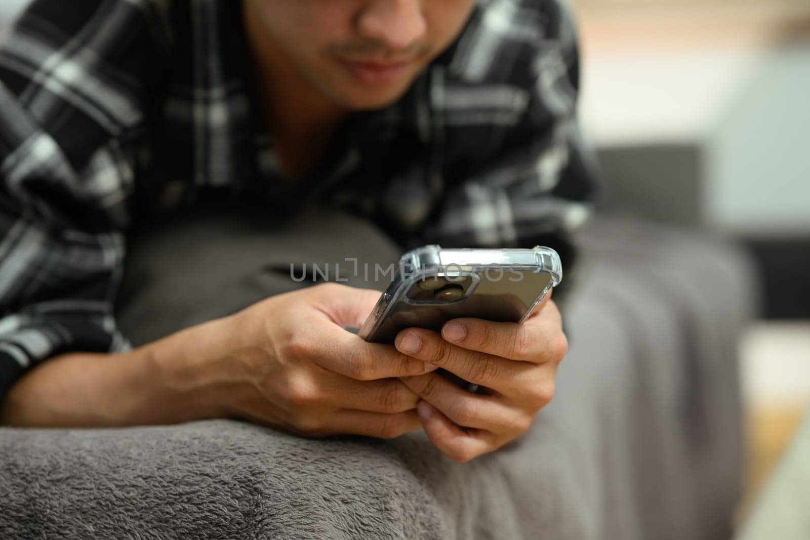 Cropped shot of young man reading messages on mobile phone lying down on sofa at home.