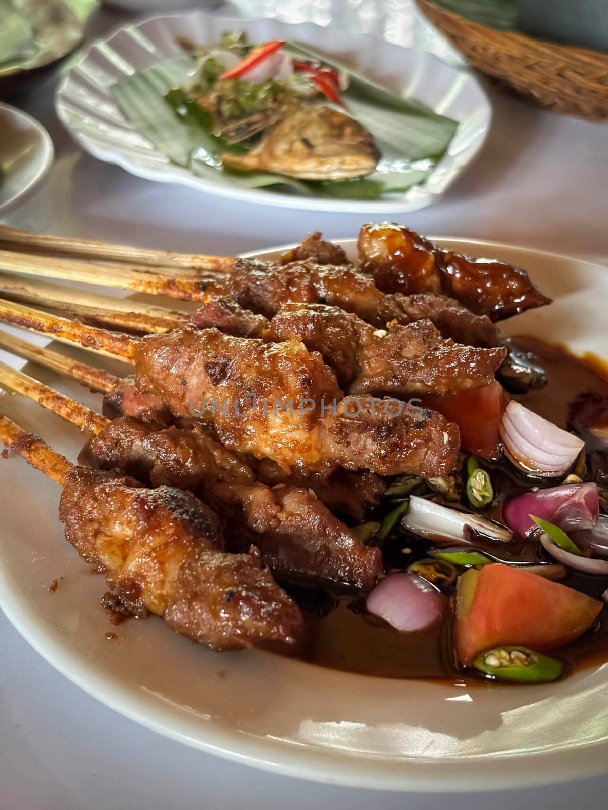 Lamb, mutton grilled skewer satay served with soy sauce sauce with sliced shallots, tomatoes, cucumber and cayenne pepper served in white plate