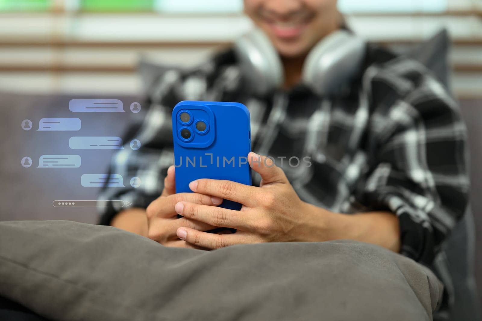 Cropped shot of smiling young man typing text message on smartphone with chatting icons.