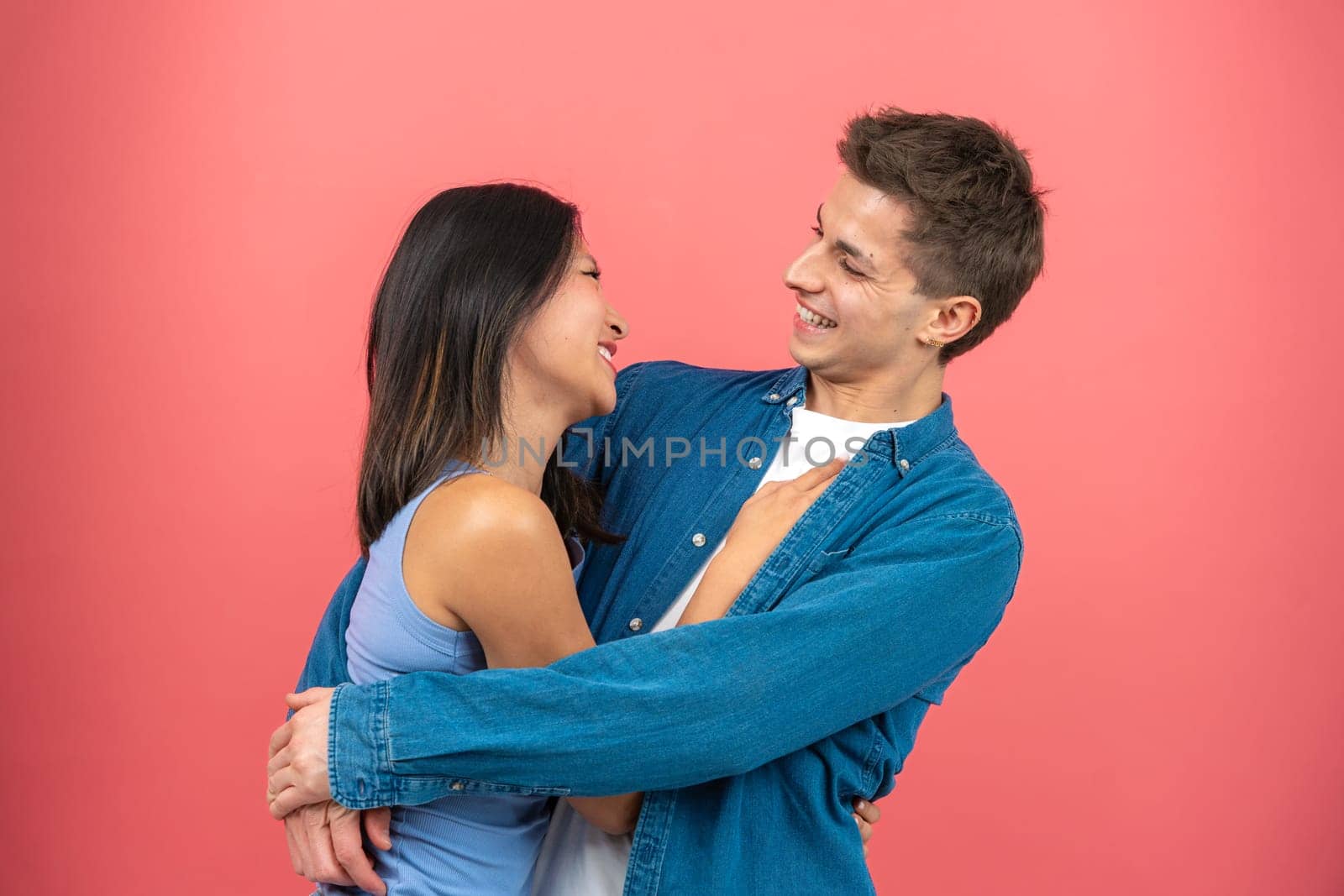 Interracial couple in a tender embrace. Studio portrait with pink background by mariaphoto3