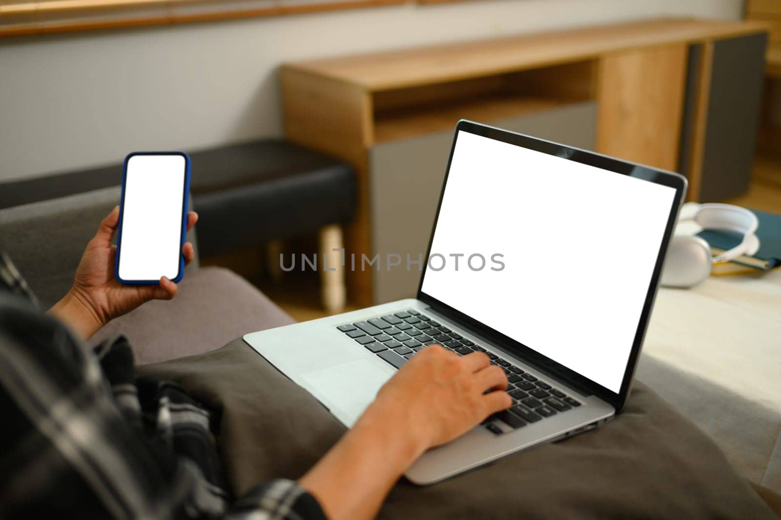 Young man using mobile phone and laptop while sitting on a sofa at home.