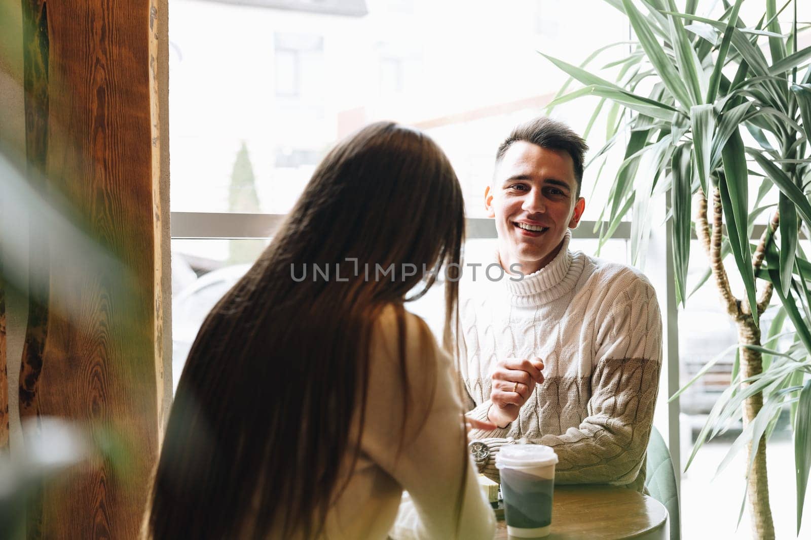 A man and woman are seated at a table engaging in conversation. They appear to be in deep discussion, leaning towards each other. The table is bare except for a few cups and plates. The man gestures with his hands while the woman listens intently.