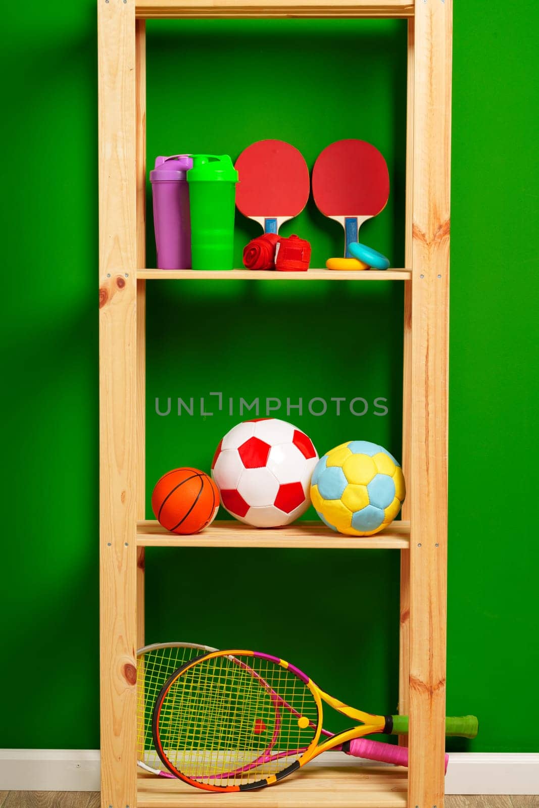 Shelves with different sports equipment against green wall by Fabrikasimf