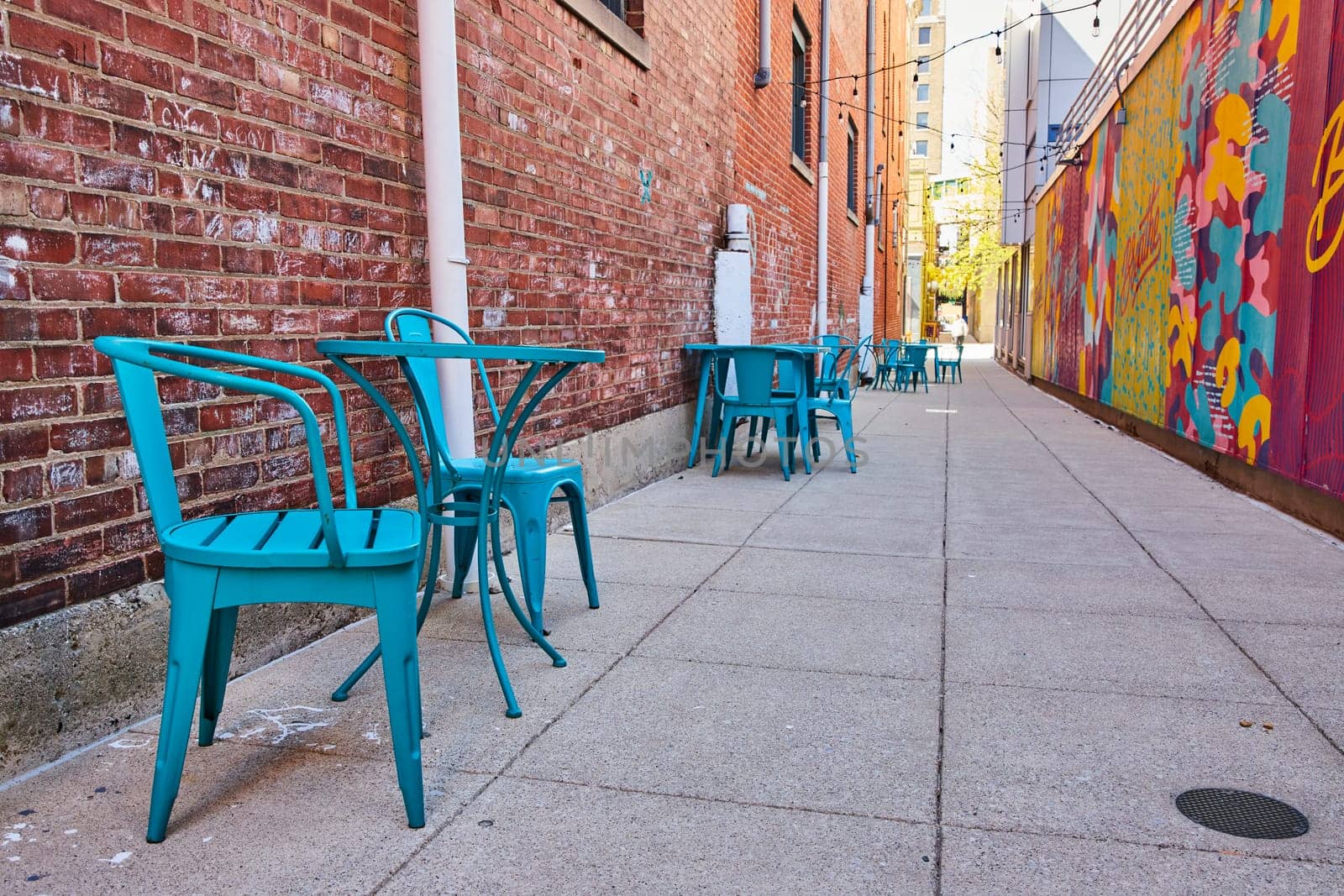 Vibrant urban cafe chairs line an alley in Fort Wayne, set against a colorful mural and historic red bricks.