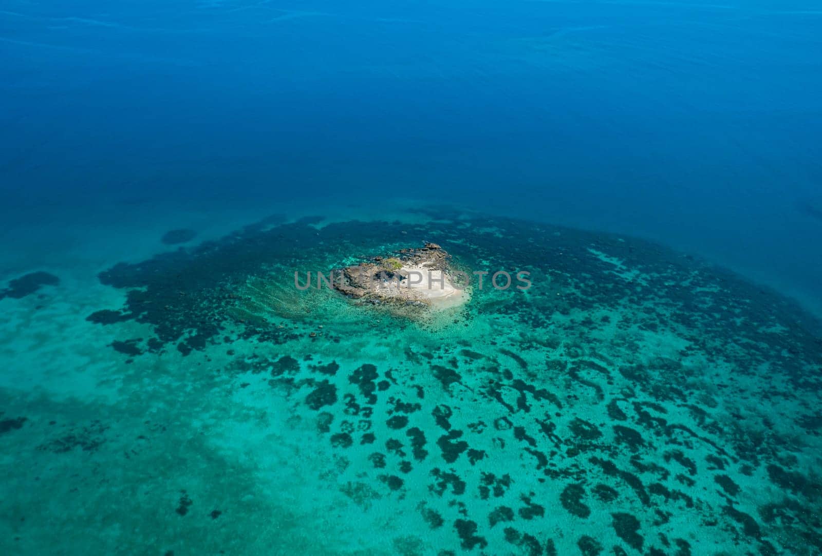 Aerial view of a small tropical island on an atoll with beautiful sandy beach surrounded by coral reef.