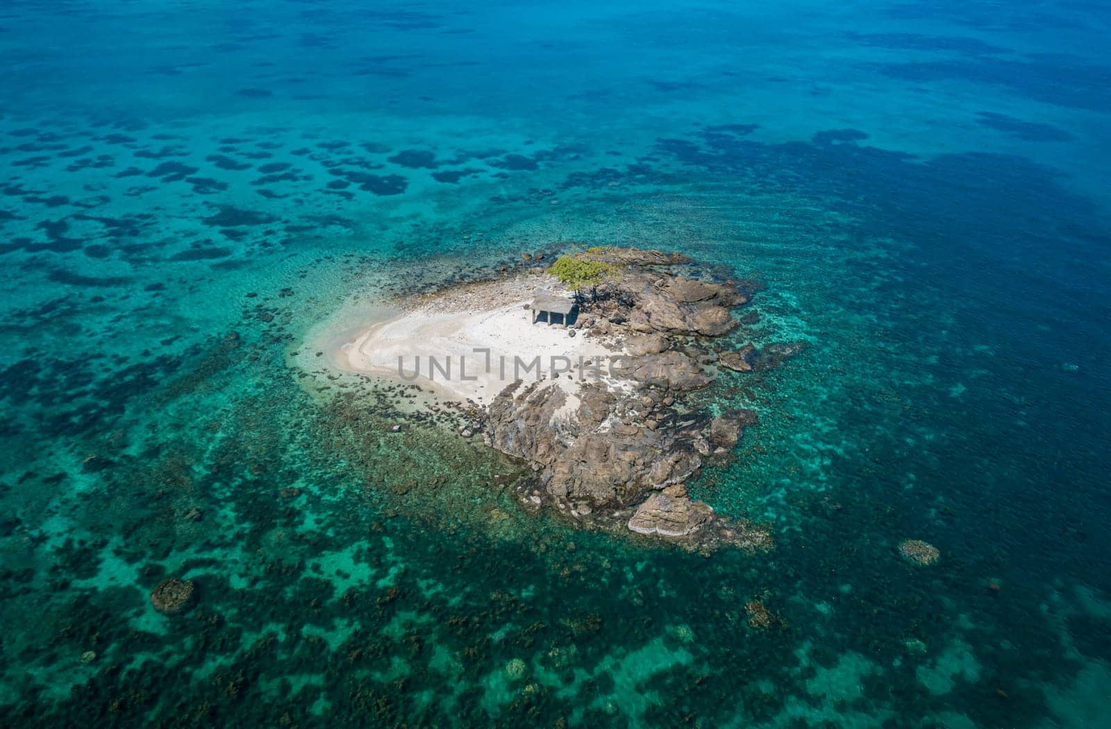Aerial view of a small tropical island on an atoll with beautiful sandy beach surrounded by coral reef.