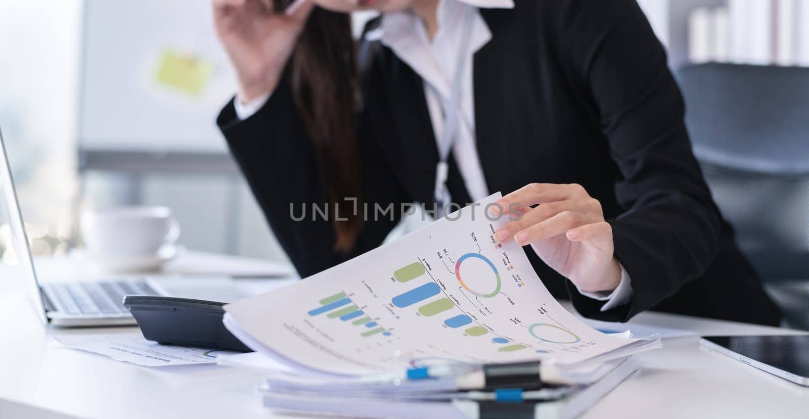 Accountant sitting with financial documents, using laptop, calculating financial and tax figures for company on table in office.