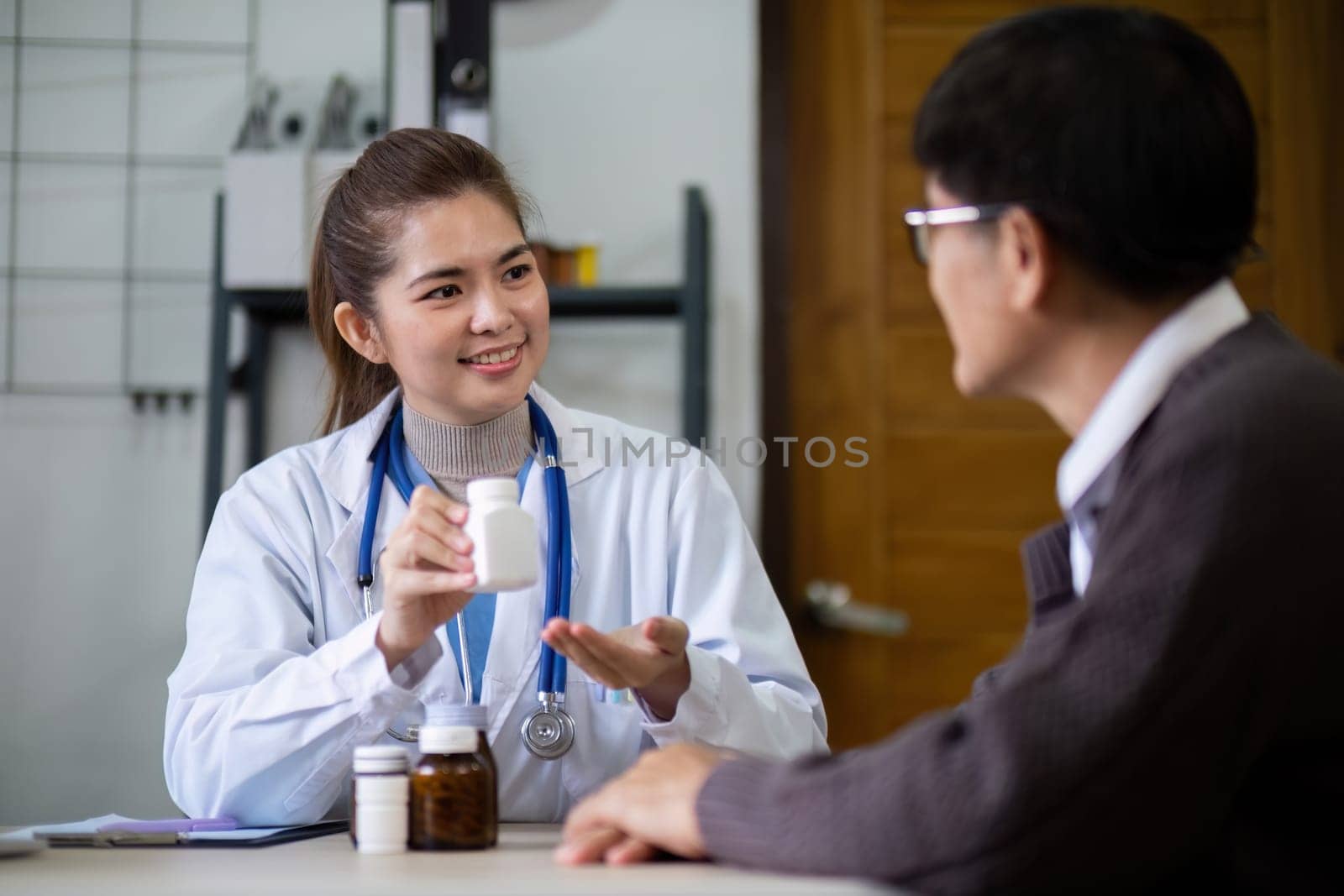 Young woman doctor sit work desk with senior old man patient prescribe drugs or pills, female nurse explain daily dosage of prescribed medicine to elderly man, elderly healthcare concept by nateemee
