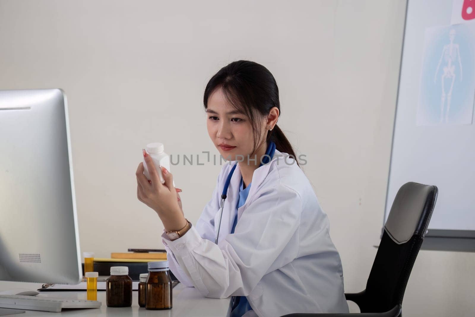 Asian Female Doctor Examining Medication Bottle in Medical Office by nateemee