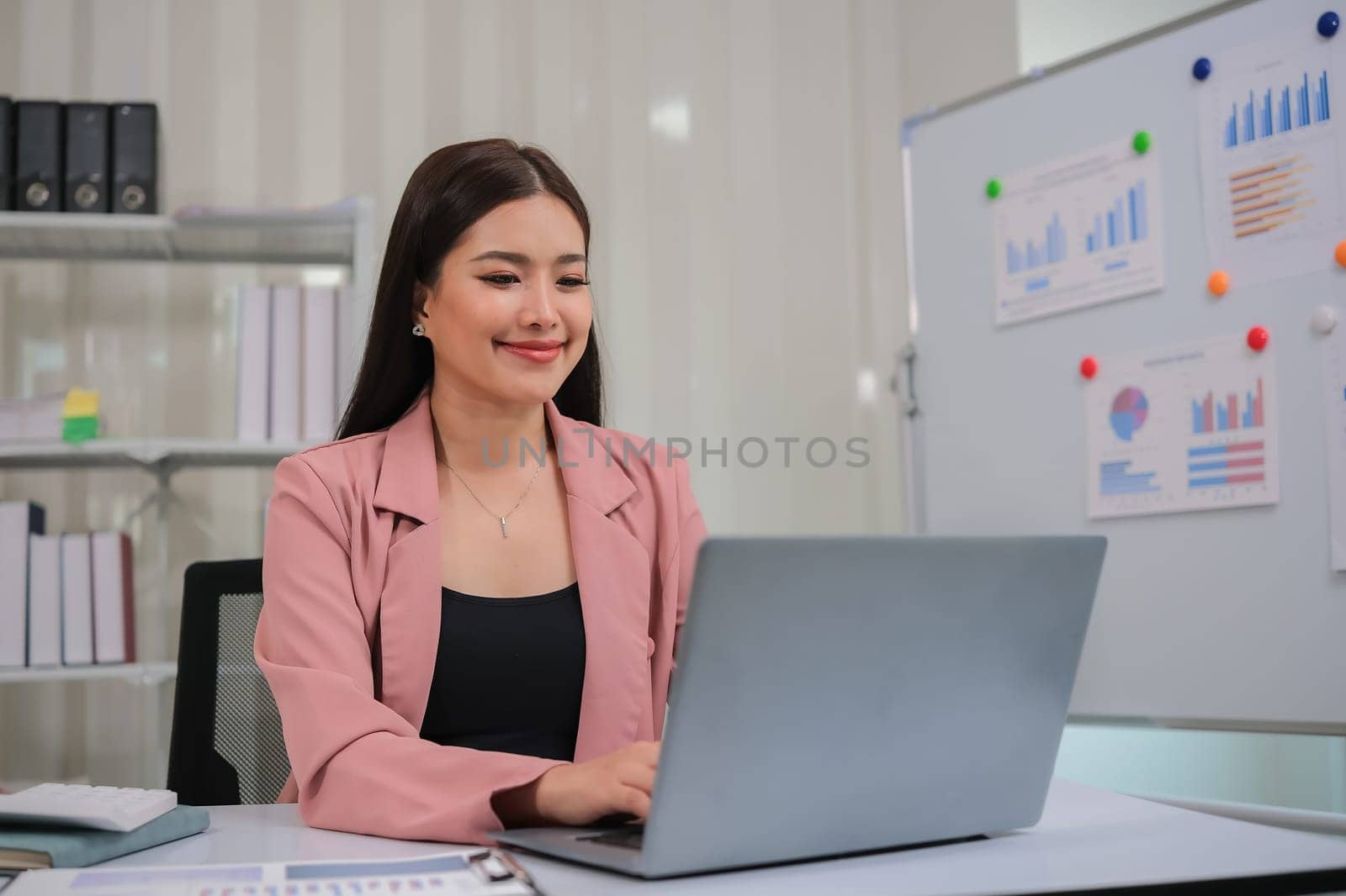 Asian businesswoman working on financial document with laptop on desk in office room.