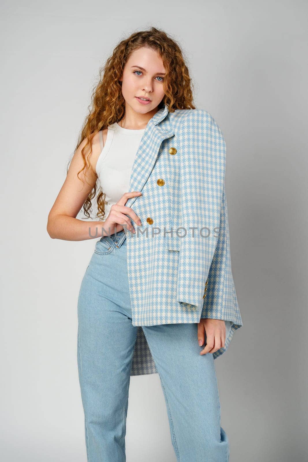 Young woman with curly hair in blue jacket posing on gray background by Fabrikasimf