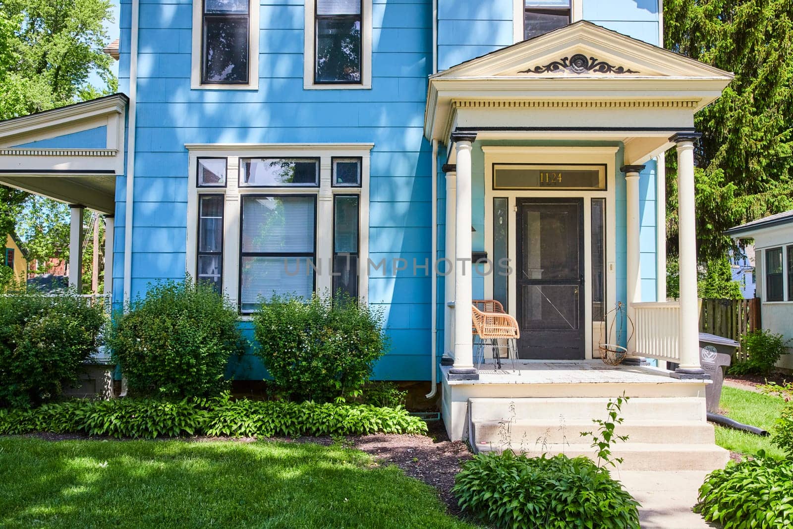 Sunny suburban charm in Fort Wayne: elegant blue home with lush greenery, perfect for a serene lifestyle.