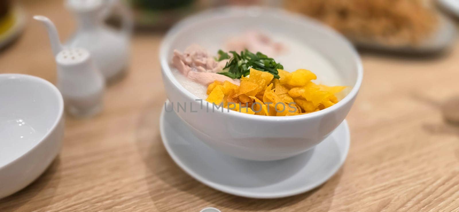 rice porridge with shredded chicken called bubur ayam served with crackers and sliced spring onion and others condiments in restaurant