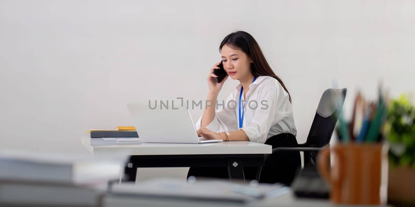 Professional Asian Businesswoman Making Phone Call at Modern Office Desk.