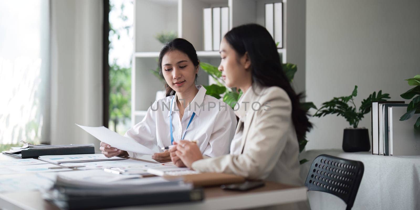 Two young businesswomen reviewing documents in a modern office.