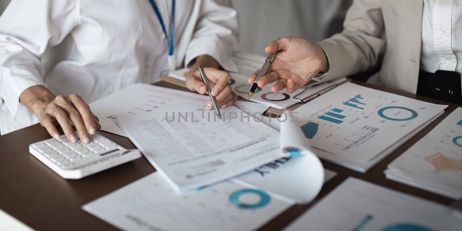Close-up of businesswomen analyzing financial documents and charts at the office.