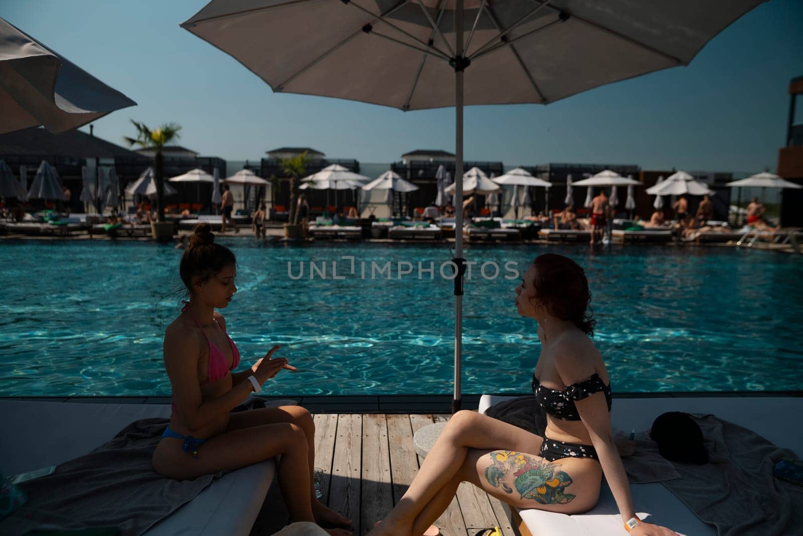 Two girlfriends in bikinis lounge poolside, enjoying the warmth of the sun. High quality photo