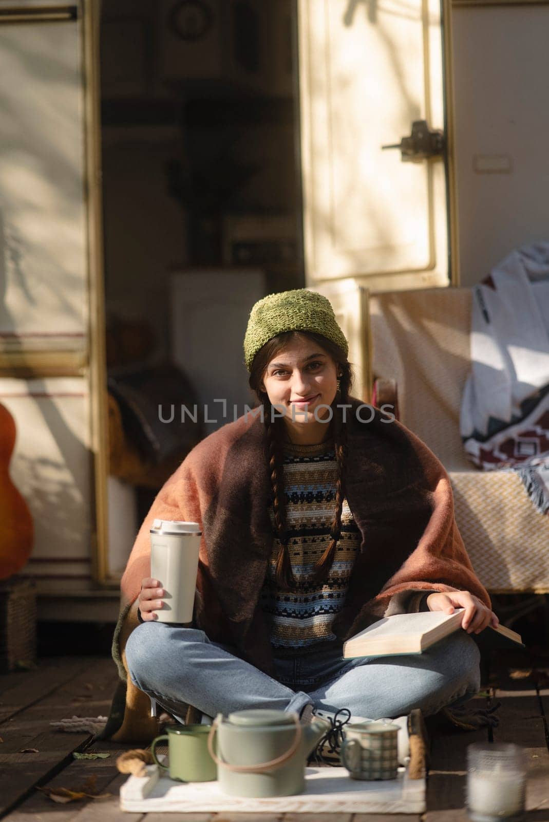 A stylish young woman in a hippie-inspired outfit enjoys a hot beverage on the house terrace. High quality photo