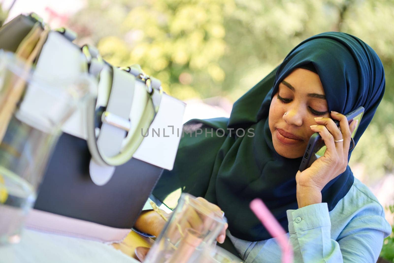 A serene African American Muslim woman in hijab engages in a peaceful conversation on her cellphone amidst the tranquil beauty of nature