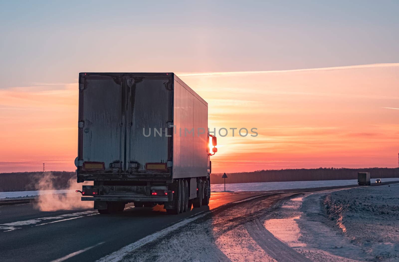 Semi truck driving along a snowy highway at sunset in winter by Busker