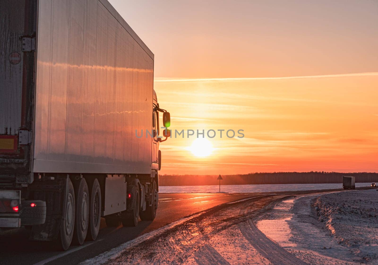 Semi truck driving along a snowy highway at sunset in winter by Busker