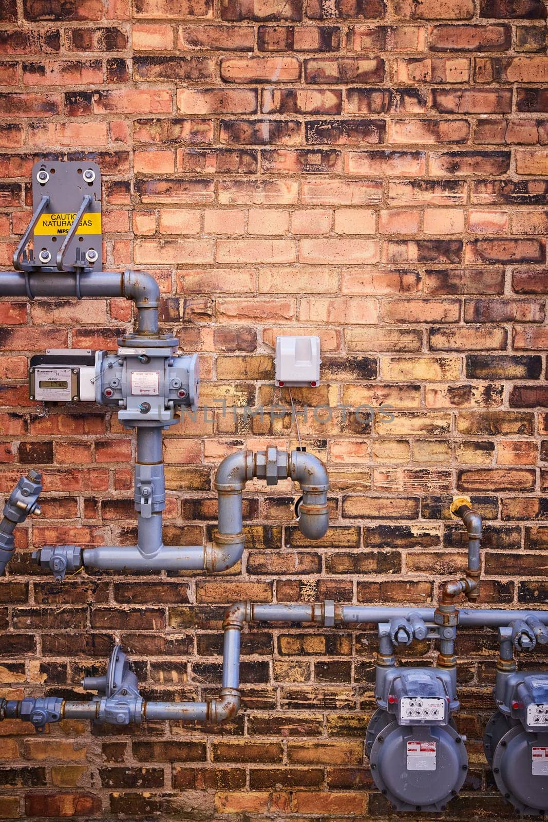 Intricate gas meters and pipes on a weathered brick wall, showcasing urban infrastructure in Fort Wayne.