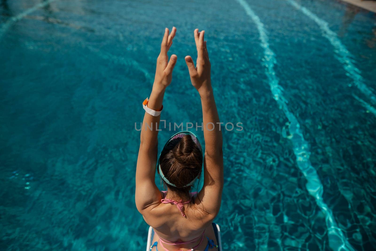 A stunning lady in a bikini reclines by the poolside, her back turned to the water. High quality photo