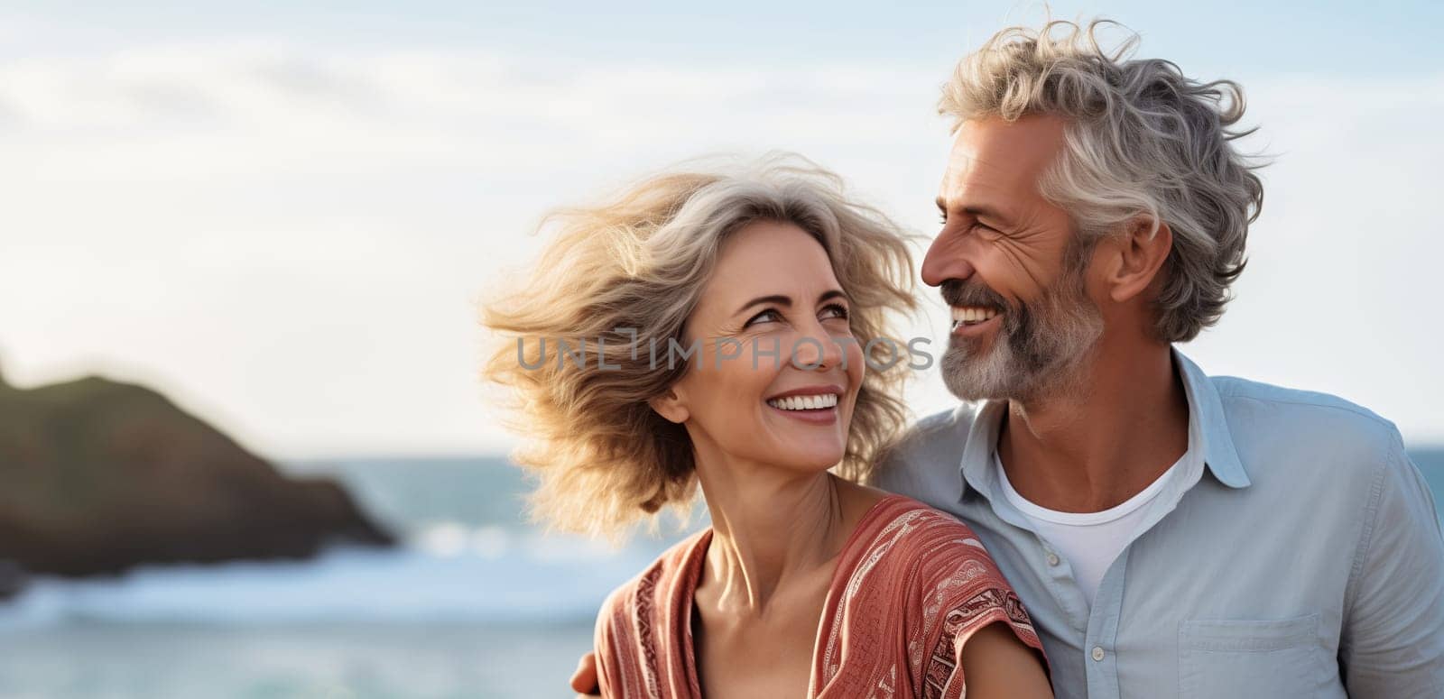 Summer portrait of happy smiling mature couple standing together on sunny coast, woman and man enjoying beach vacation at sea