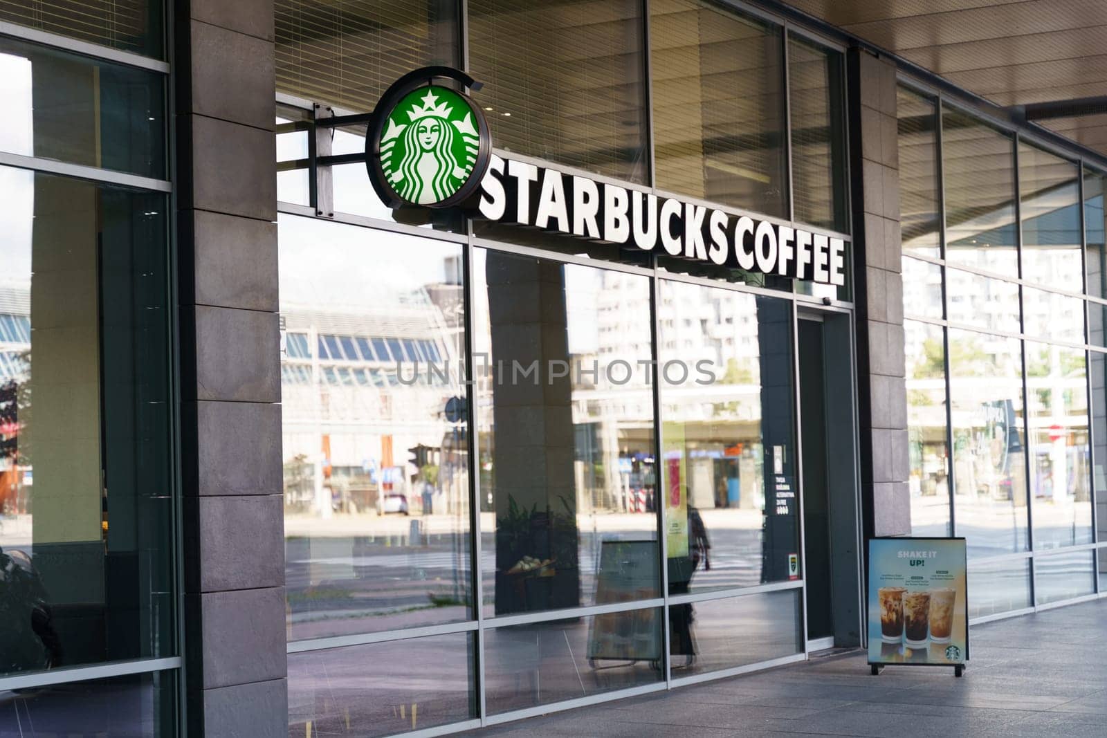 Wroclaw, Poland - August 4, 2023: A modern Starbucks Coffee shop with glass windows located on a busy city street. The view through the windows shows an urban scene with buildings and street activity in the background.