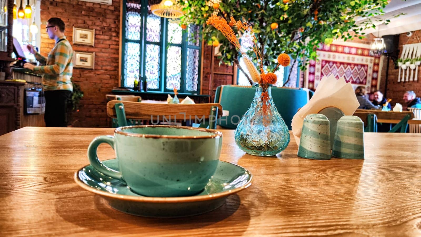 A ceramic teacup rests on a table with cafe interior in soft focus behind