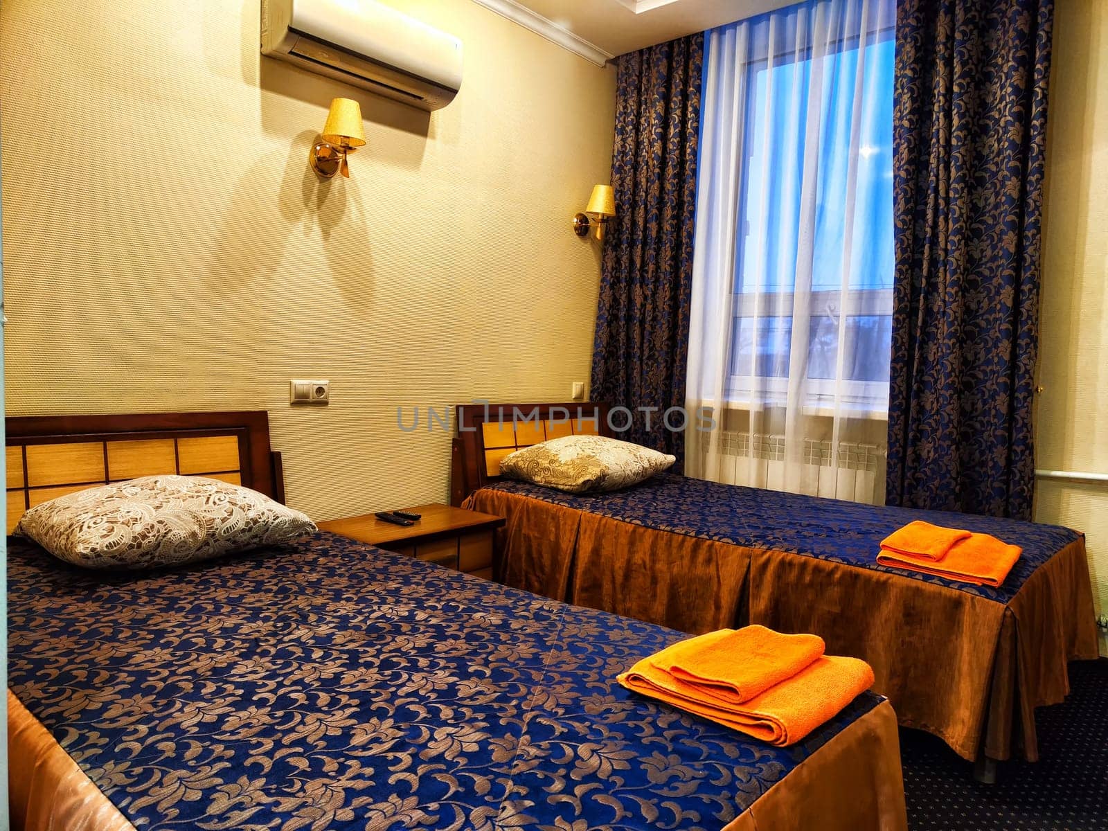 Twin Beds in Cozy Hotel Room. Two single beds with blue bedding and orange towels in a hotel room