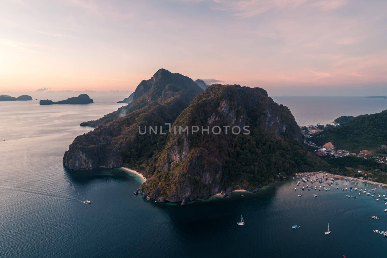 Aerial view of cliffs in the sea, yachts are sailing nearby, mountains covered with tropical forest. El Nido, Palawan, Philippines. by Busker