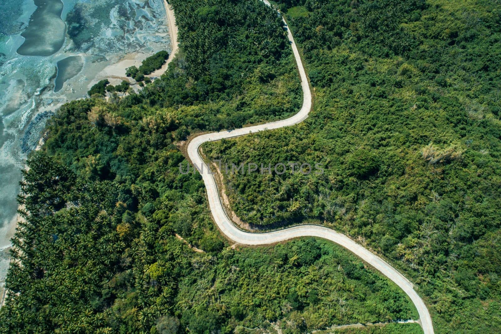 Aerial view of winding countryside road passing through green hills. Summer and travel vacation concept. by Busker