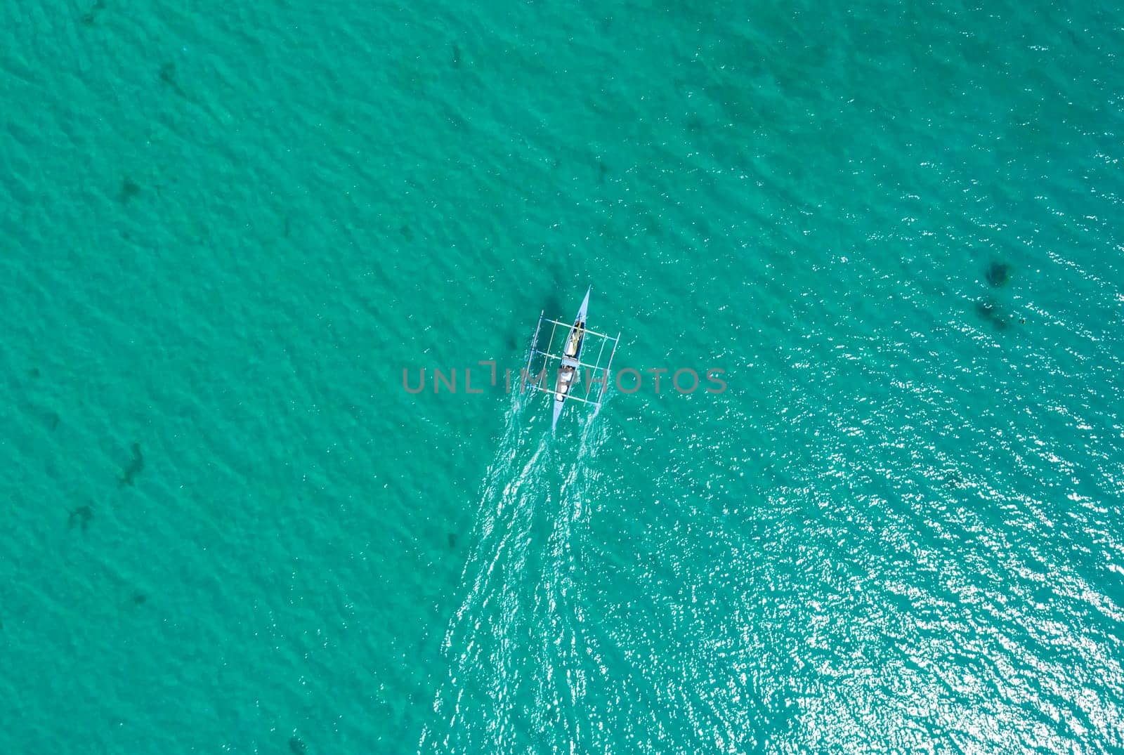 Aerial top view of Banca boat floating in open sea with clear and turquoise water on sunny day . Tropical landscape.