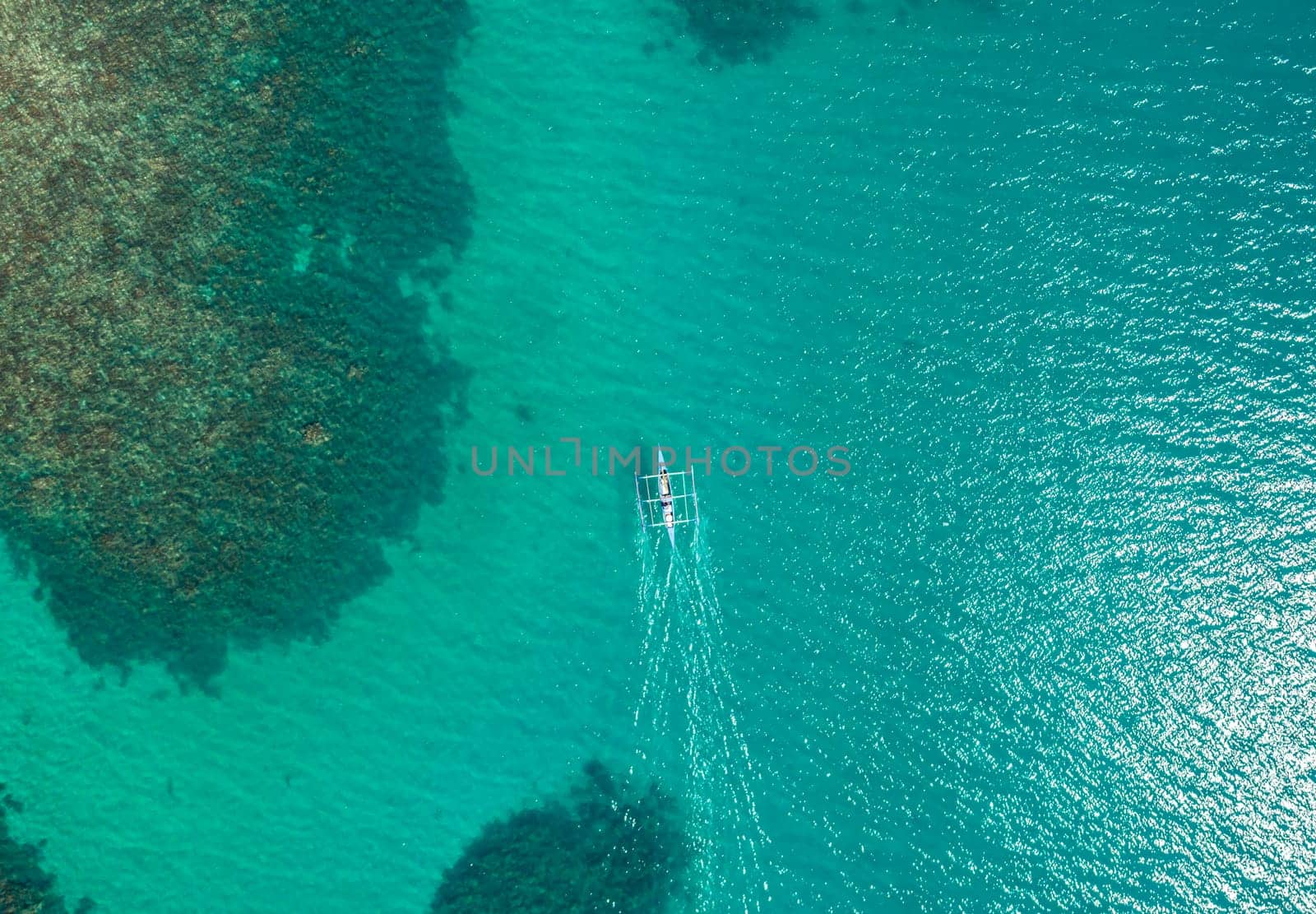 Aerial top view of Banca boat floating in open sea with clear and turquoise water on sunny day . Tropical landscape.