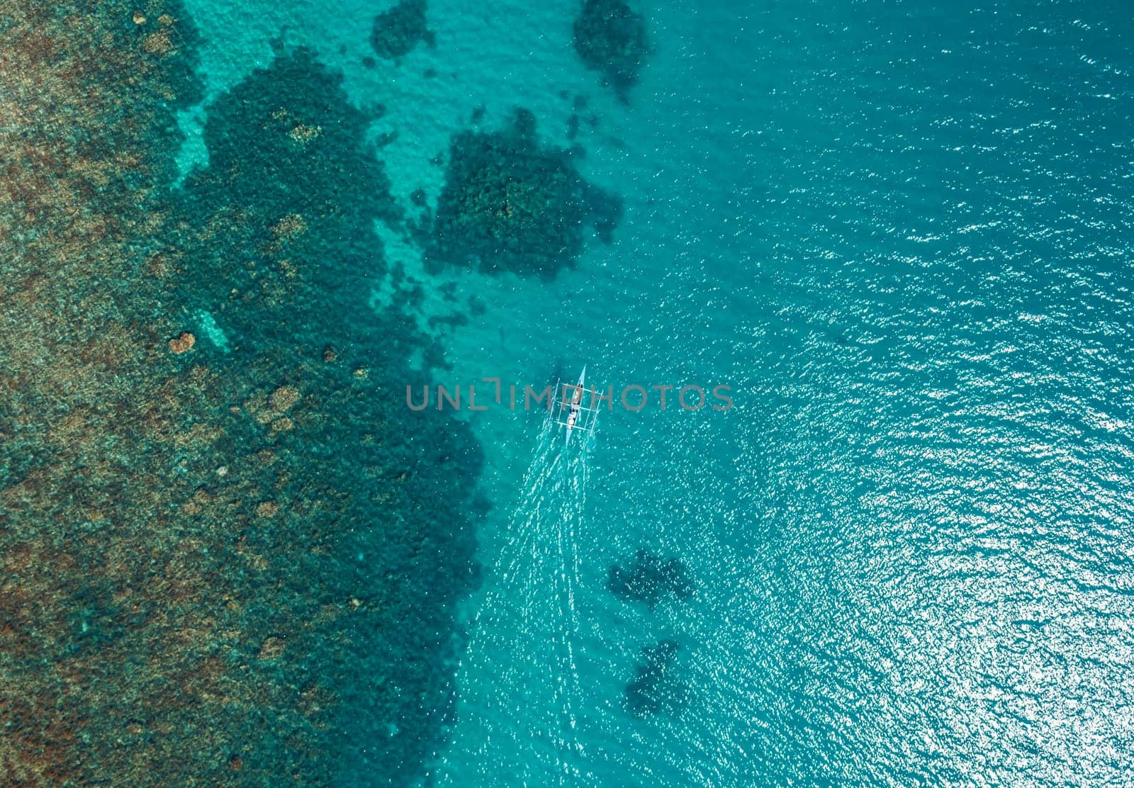 Aerial top view of Banca boat floating in open sea with clear and turquoise water on sunny day . Tropical landscape.