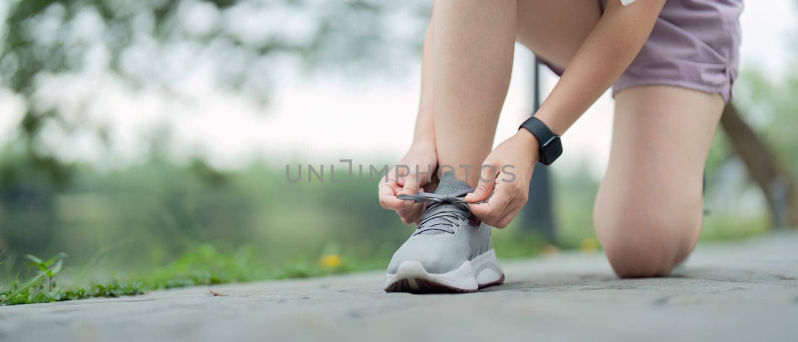 Young woman tying shoelace in the park. Sport and fitness concept by nateemee