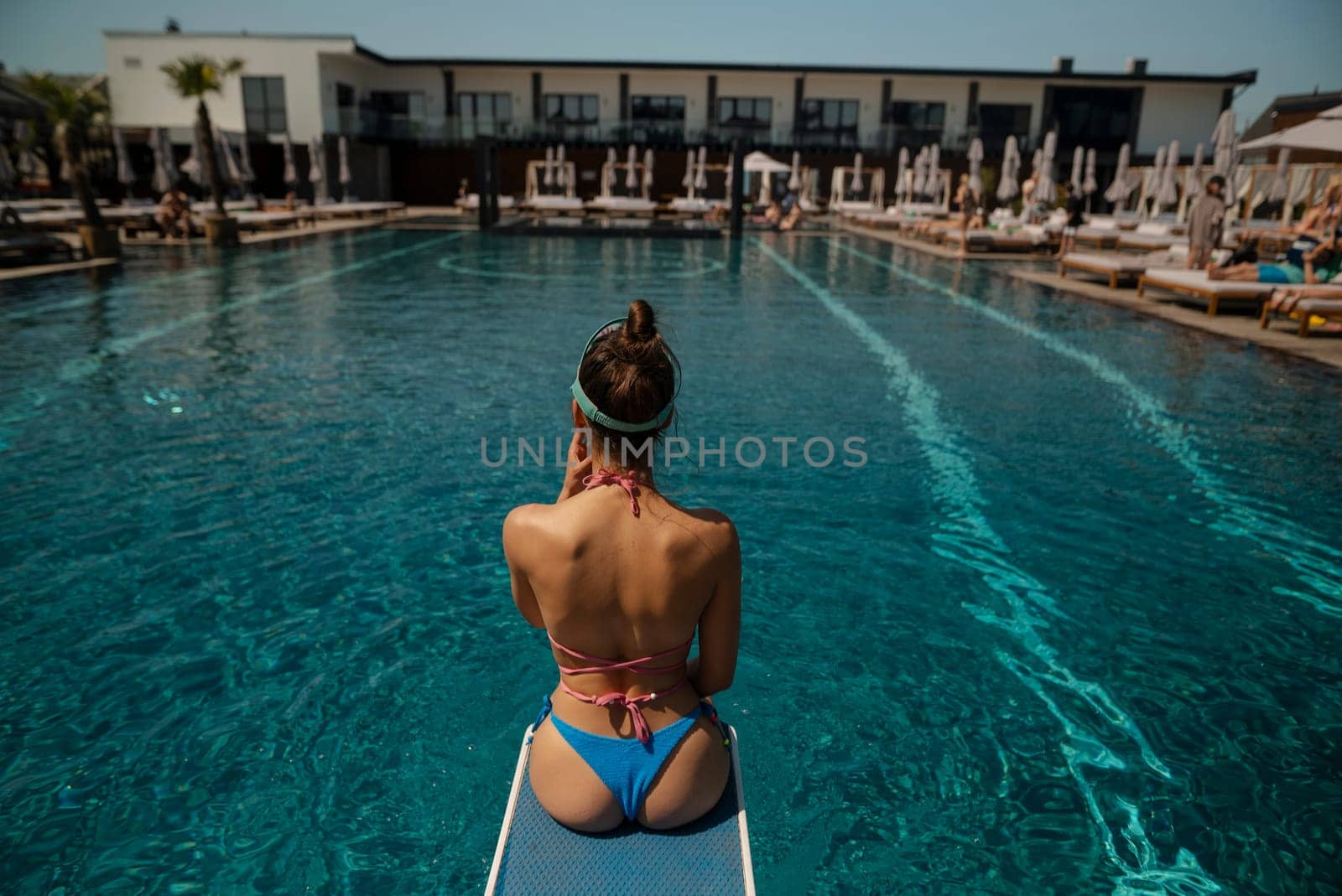 An enchanting woman in swimwear lounges by the pool, with her back to the pool. High quality photo