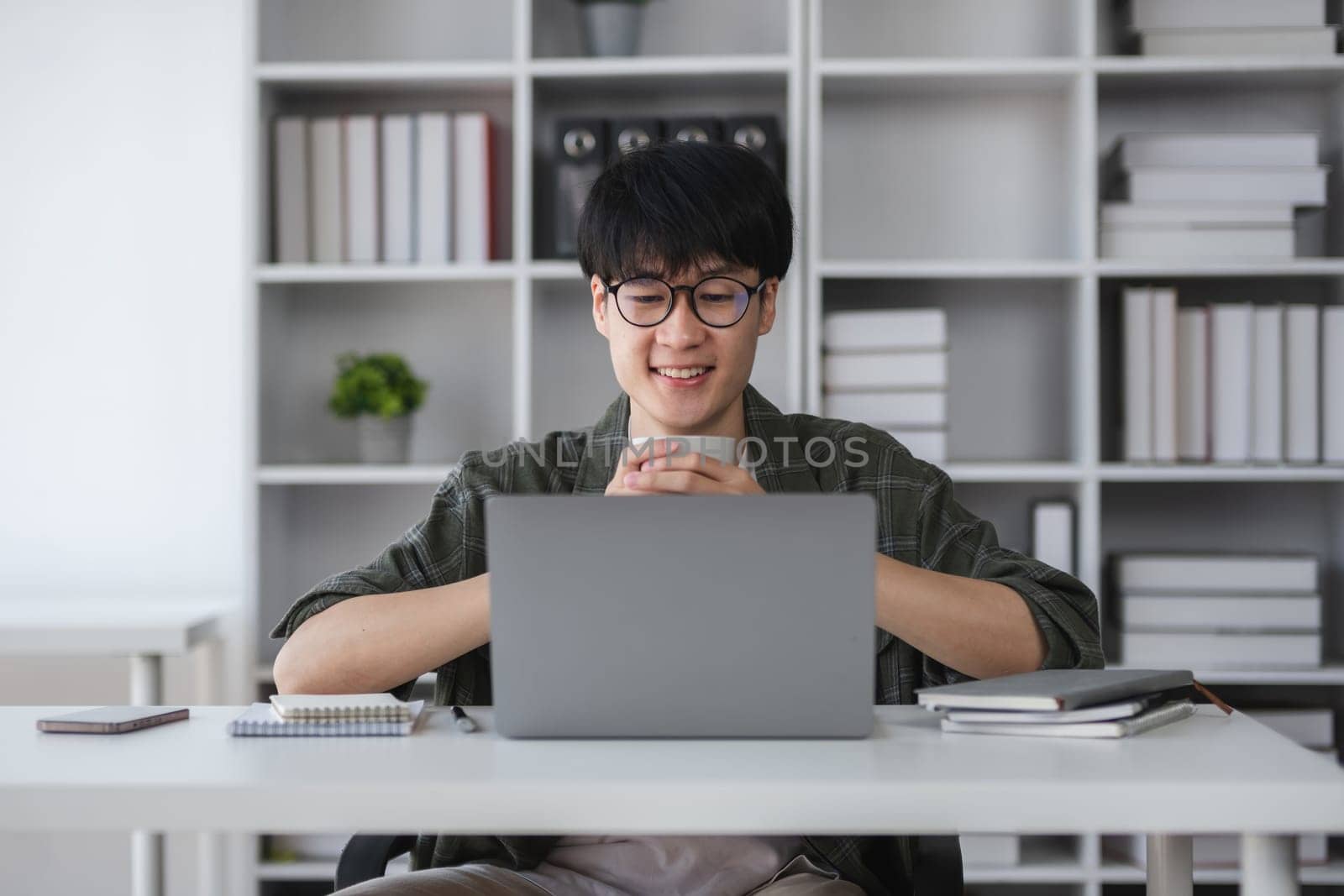 Young Asian student boy in private clothes studying online with laptop at home. by wichayada