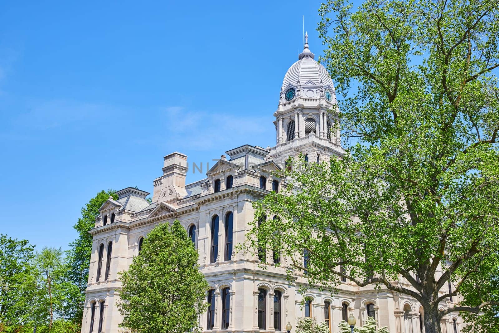 Bright sunlight bathes the classical architecture of Kosciusko County Courthouse against a clear blue sky.