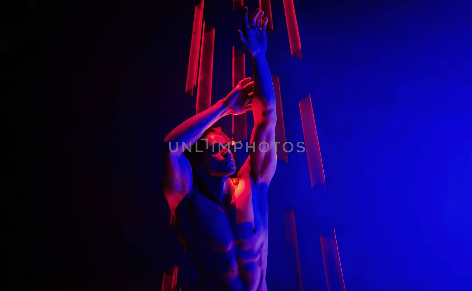 Sporty handsome man with long hair, naked torso abs portrait under colorful illumination, laser light, neon smoke club. Projection illusion mapping. Futuristic model.