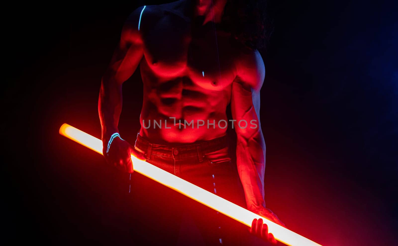 Sporty handsome man with neon light tube under colorful illumination, laser, smoke room. Muscular strong guy with naked torso abs. Projection illusion mapping. Futuristic model.