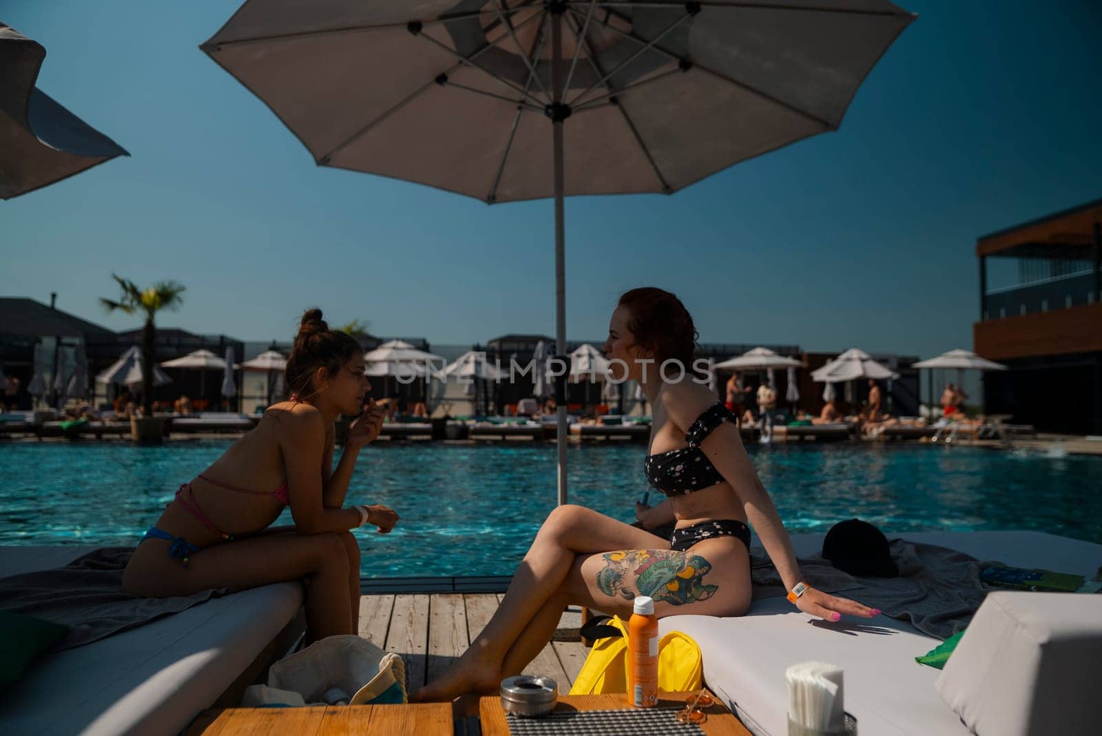 Two young friends in swimsuits lounge by the poolside, enjoying each other's company. by teksomolika