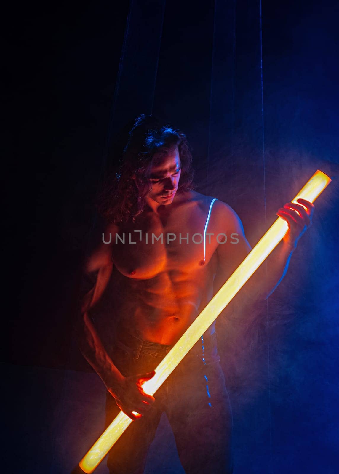 Sporty handsome man with neon light tube under colorful illumination, laser, smoke room. Muscular strong guy with naked torso abs. Projection illusion mapping. Futuristic model.