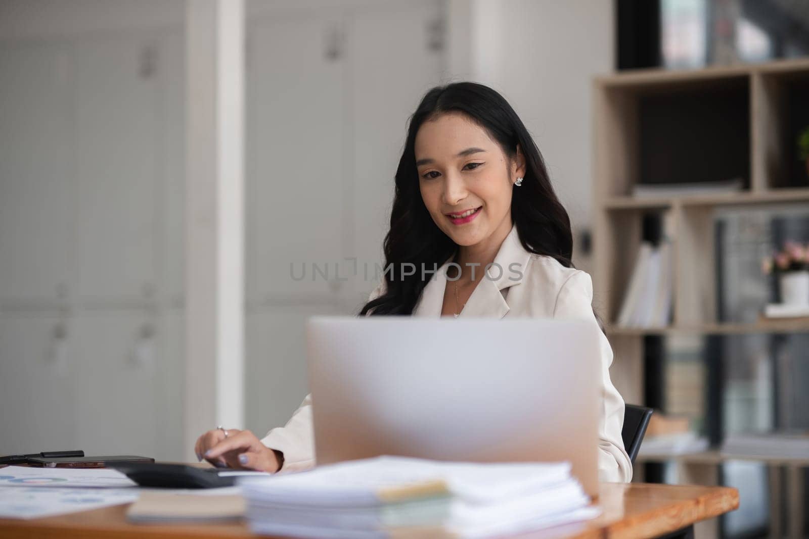 Asian businesswoman working on financial document with laptop on desk in office room by wichayada