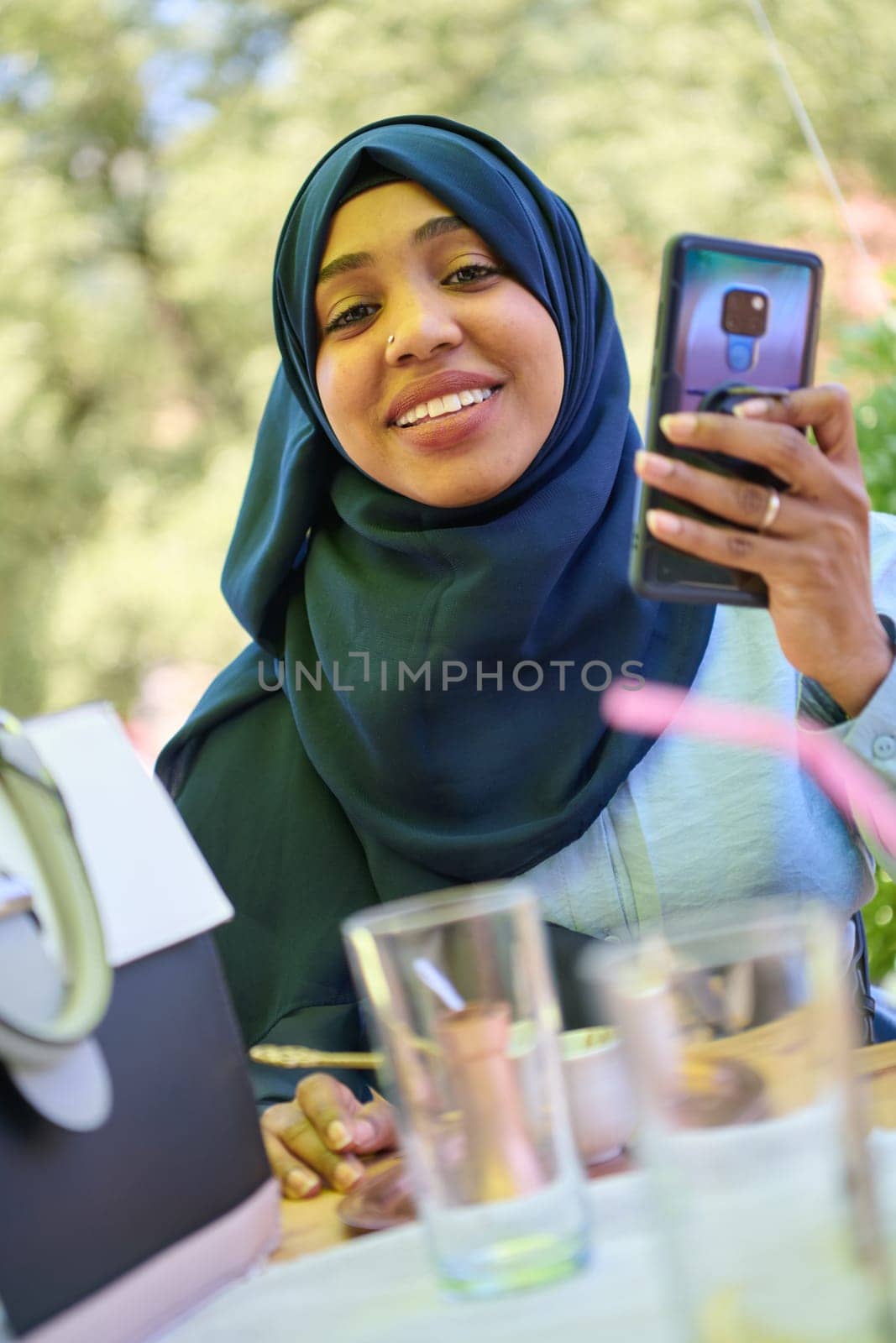A serene African American Muslim woman in hijab engages in a peaceful conversation on her cellphone amidst the tranquil beauty of nature