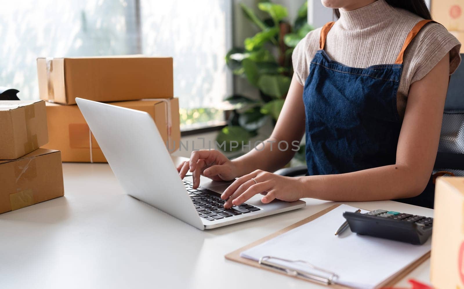 Asian women packing boxes and using a tablet in a home office. Concept of small business and e-commerce.