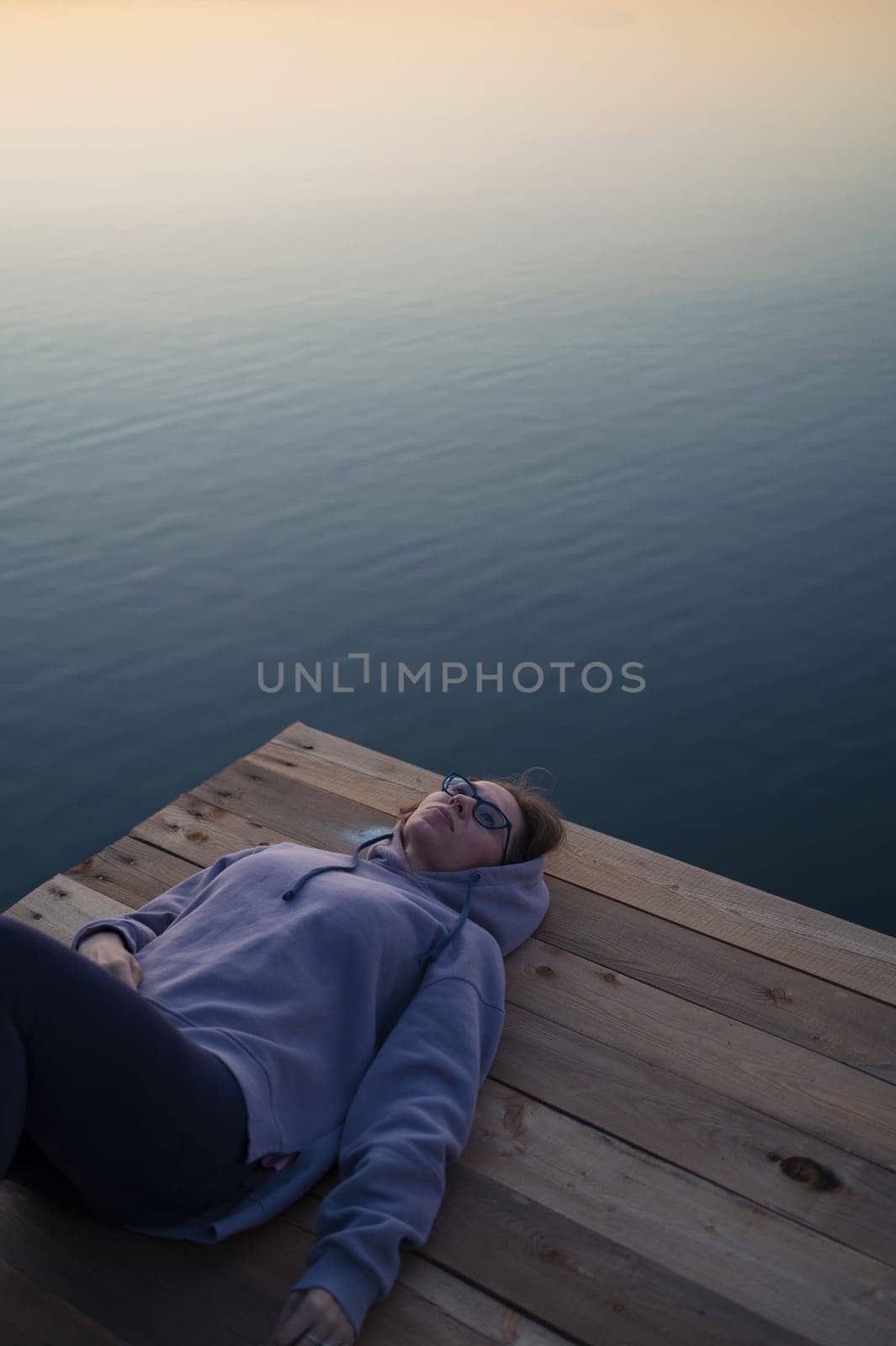 Woman lying down on the pier at lake, closeup portrait, summer sunset